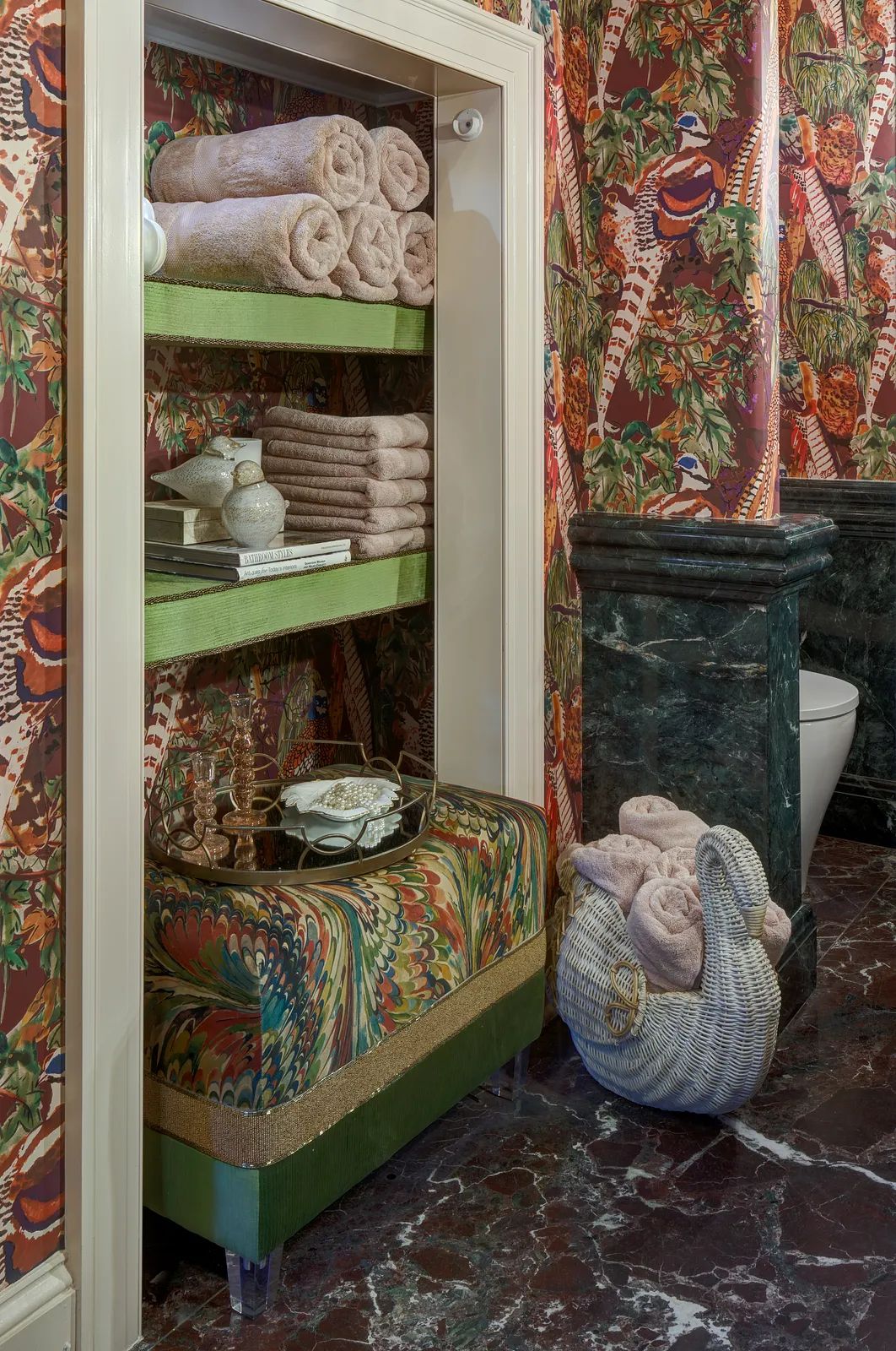 Powder room with patterned wallpaper, green towel shelf, decorative bench, and marble floor.