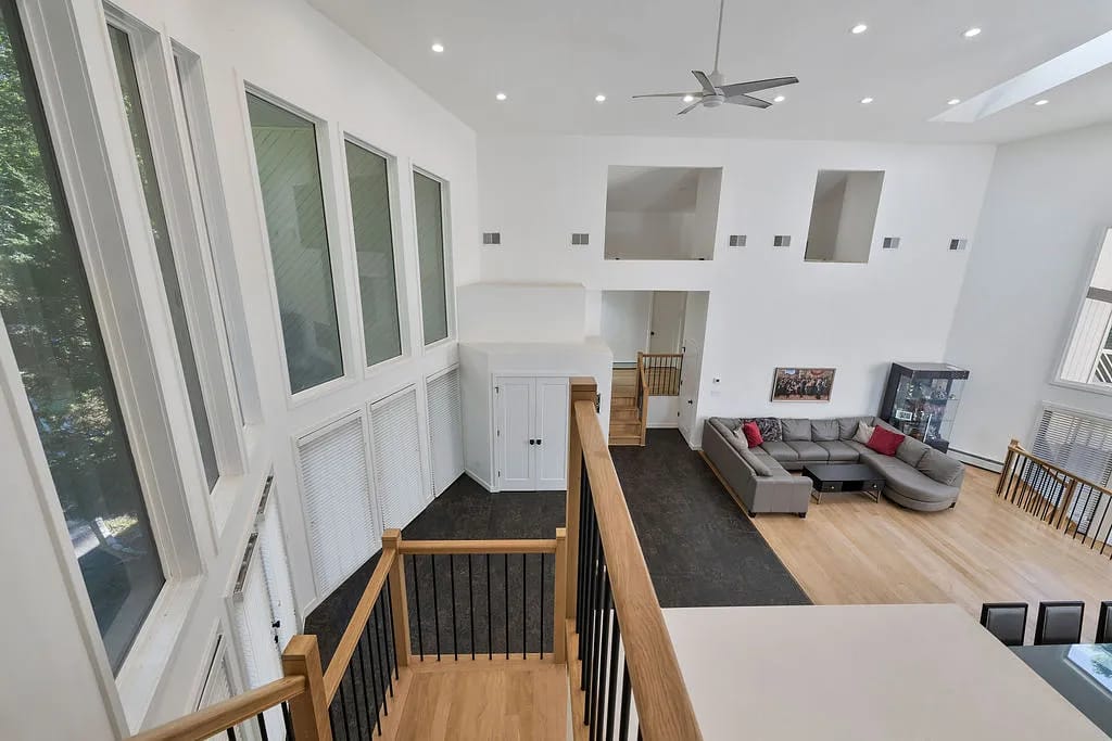 Living room with gray sectional sofa, large windows, hardwood flooring, display cabinet, and high ceilings.