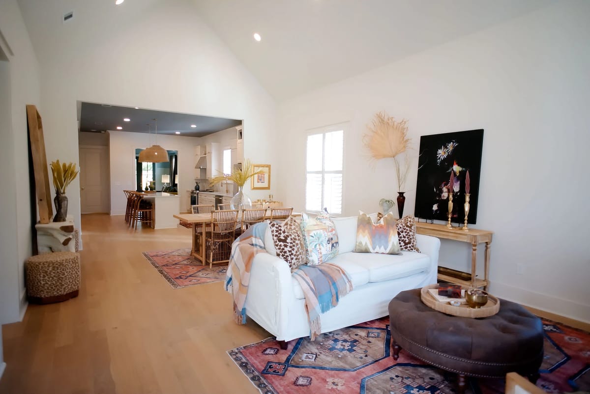 Living room with white sofa, round ottoman, area rug, wall art, and open dining area.