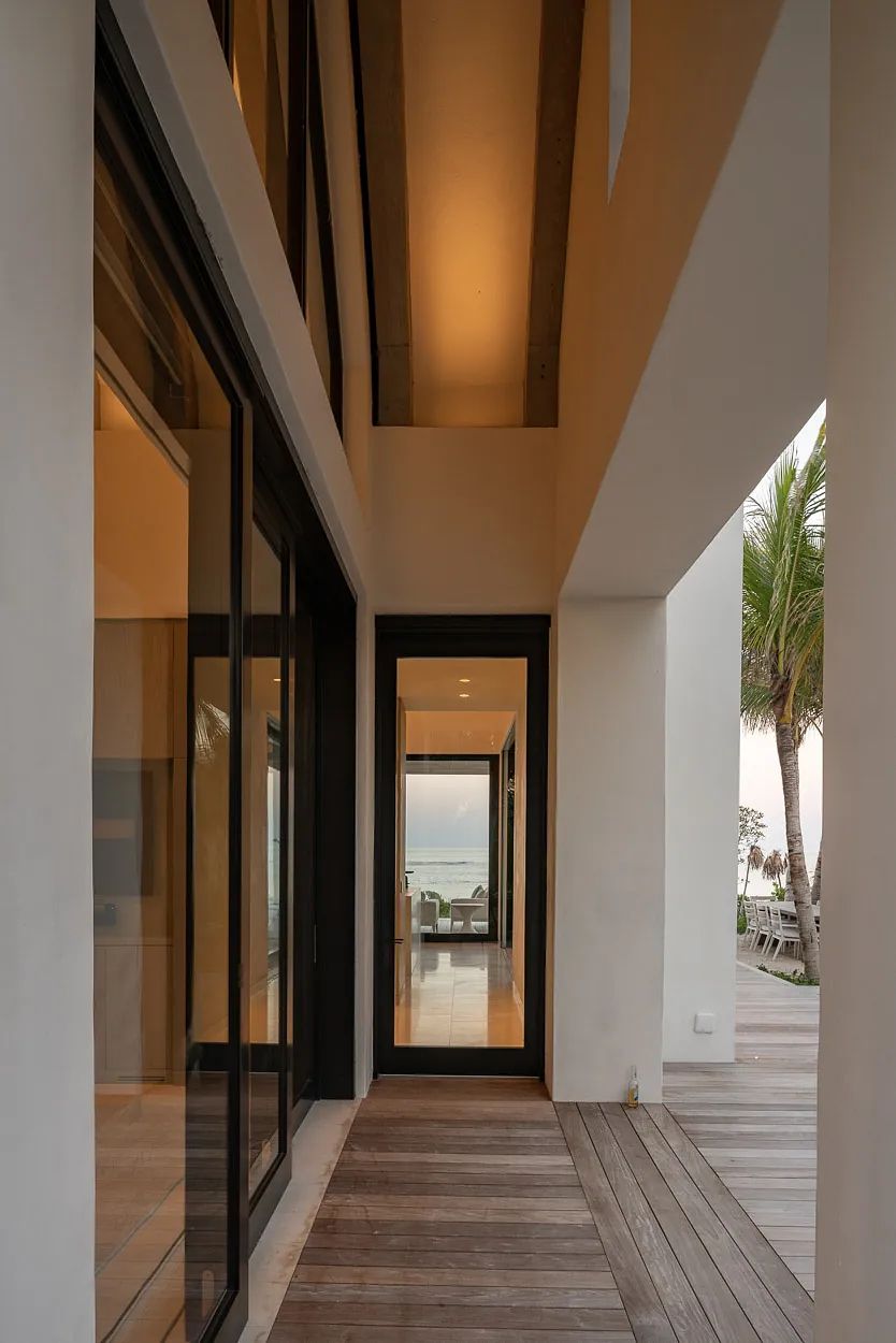 Hallway with glass doors, wooden flooring, and natural light leading to another door.