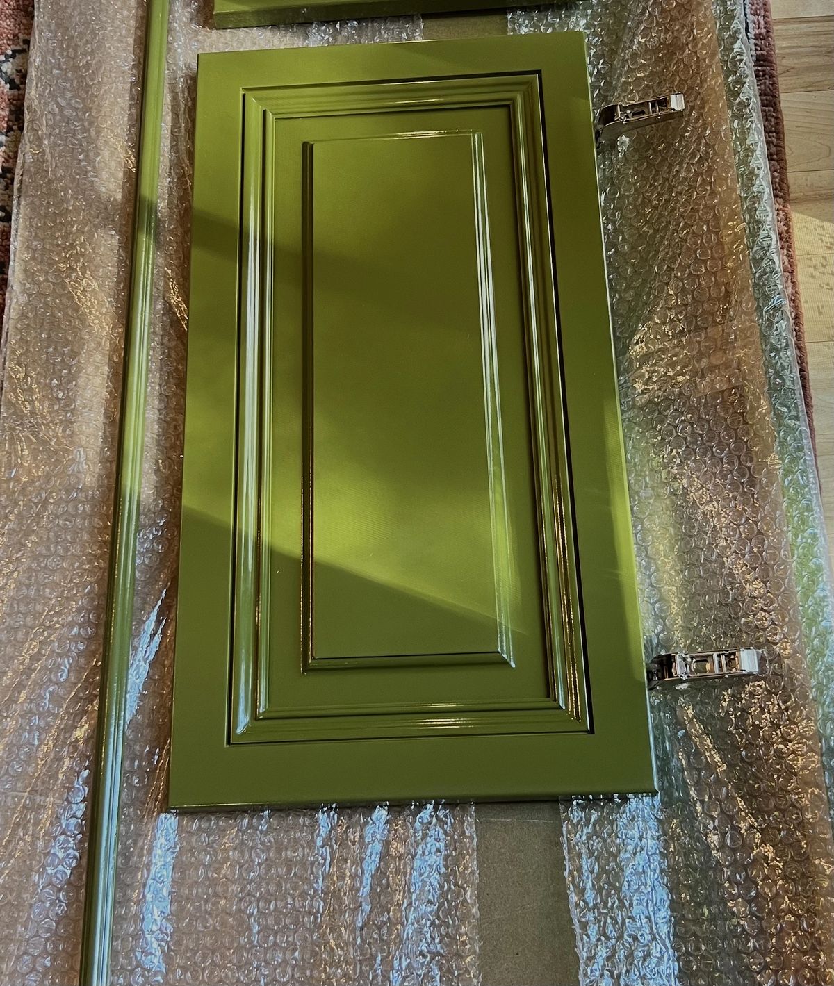 Green cabinet door with raised panel design on bubble wrap surface.