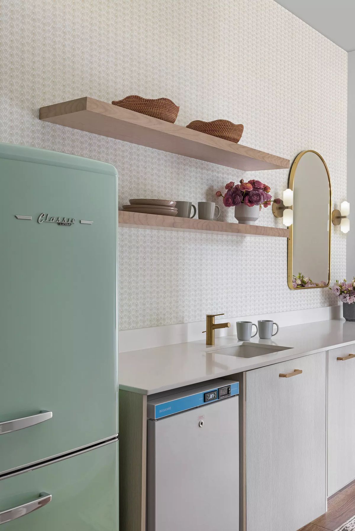 Kitchen with mint green refrigerator, white countertop, sink, wooden shelves, and an oval mirror with wall sconces.