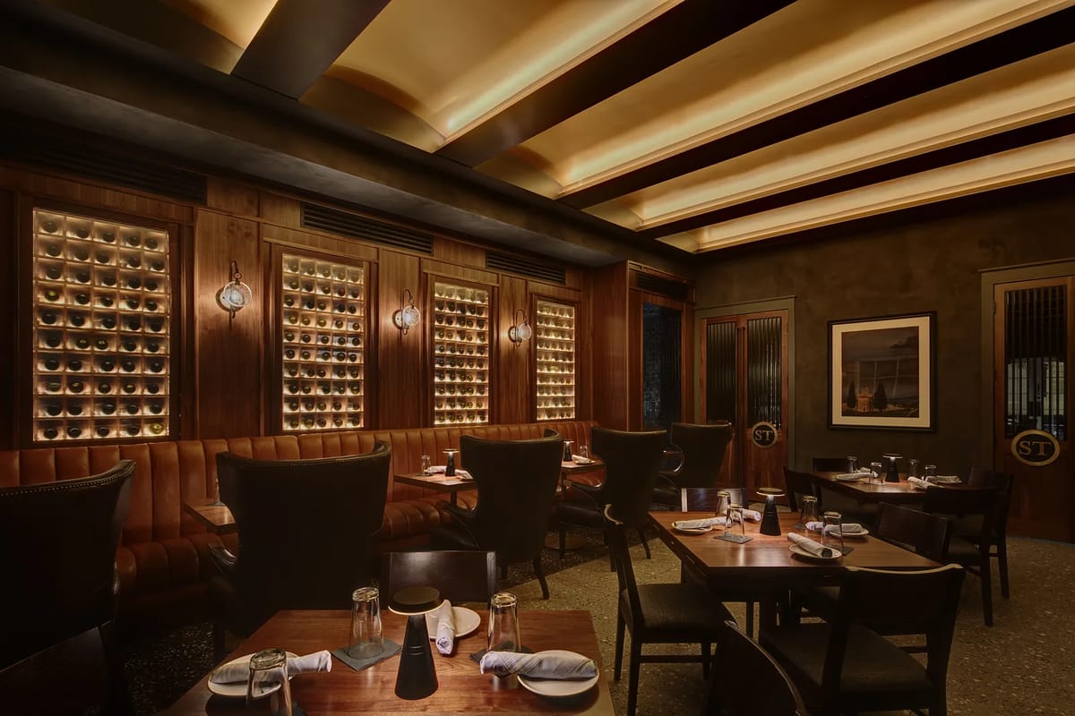 Dining room with wood tables, leather seating, wine storage, and dark wood beams in ceiling.