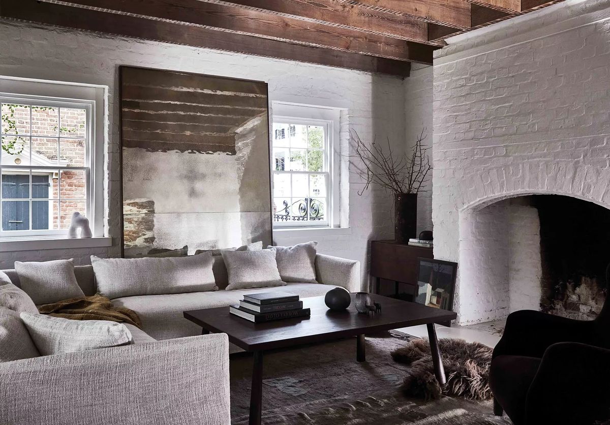 Living room with sectional sofa, wood coffee table, area rug, windows, brick fireplace, and wooden beams.