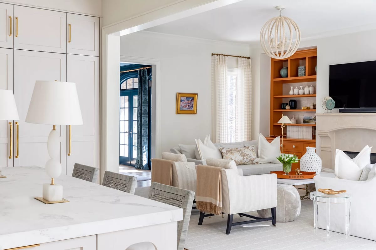 Living room with white sofa, beige armchairs, coffee table, bookshelf, and natural light from large windows