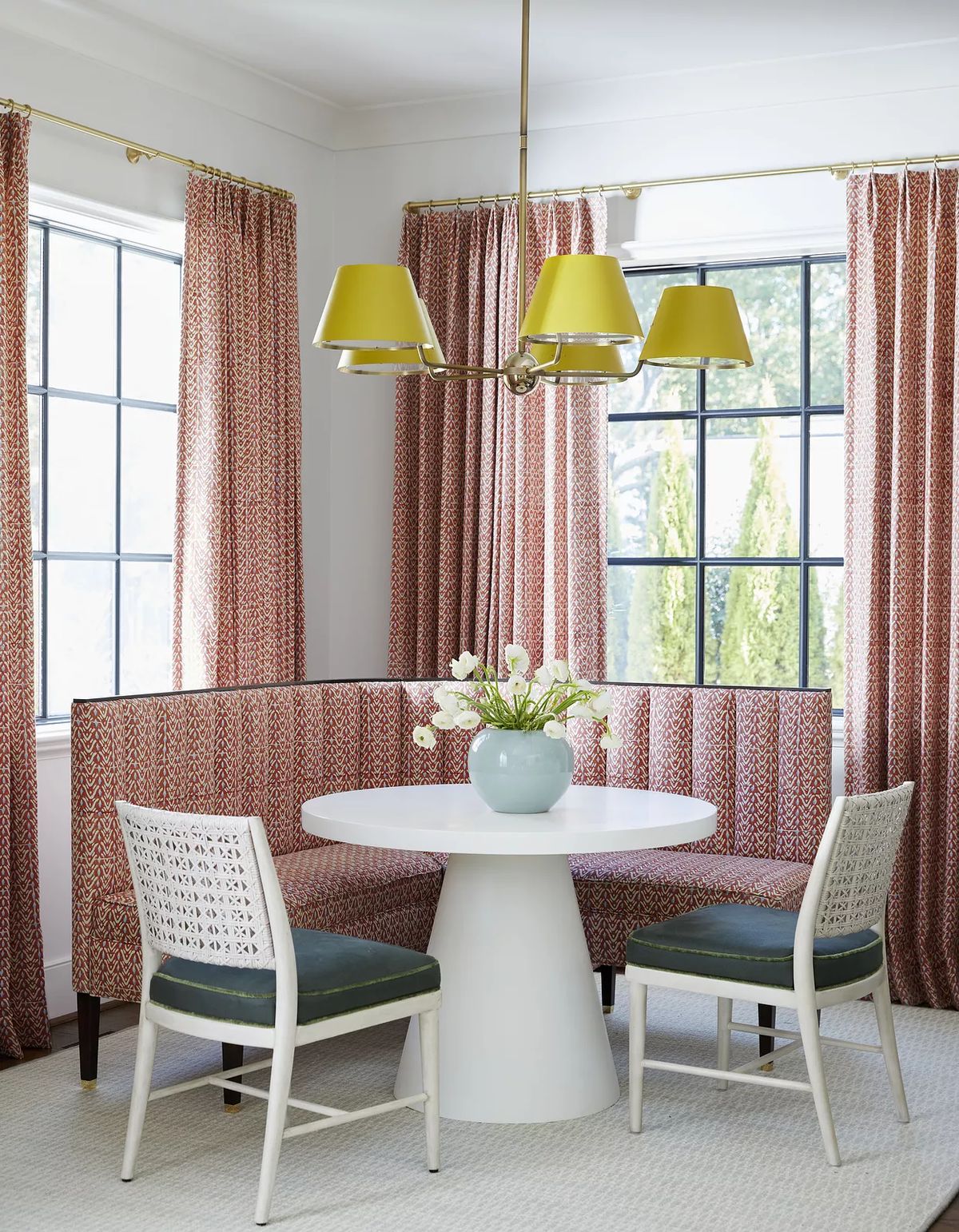 Dining room with round white table, green chairs, upholstered bench, and chandelier with green shades.