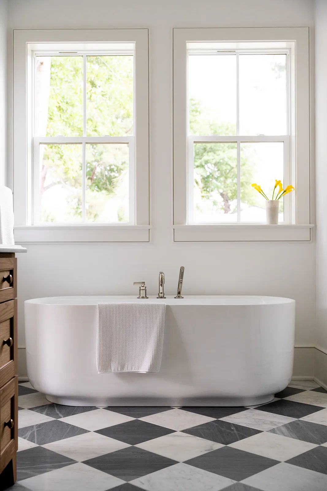 Bathroom with freestanding white bathtub, checkered floor, windows, and a potted plant.