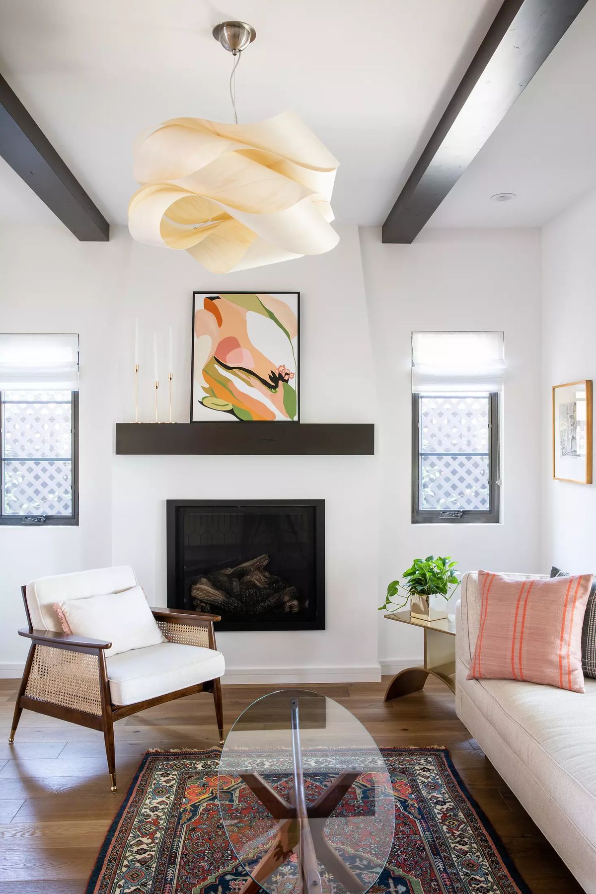 Living room with white sofa, wood chair, round glass table, rug, wall fireplace, and windows with shades