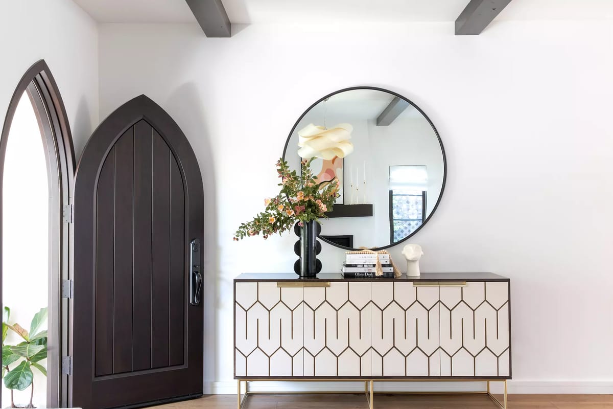 Foyer with arched door, round mirror, geometric console table, and decorative flowers.