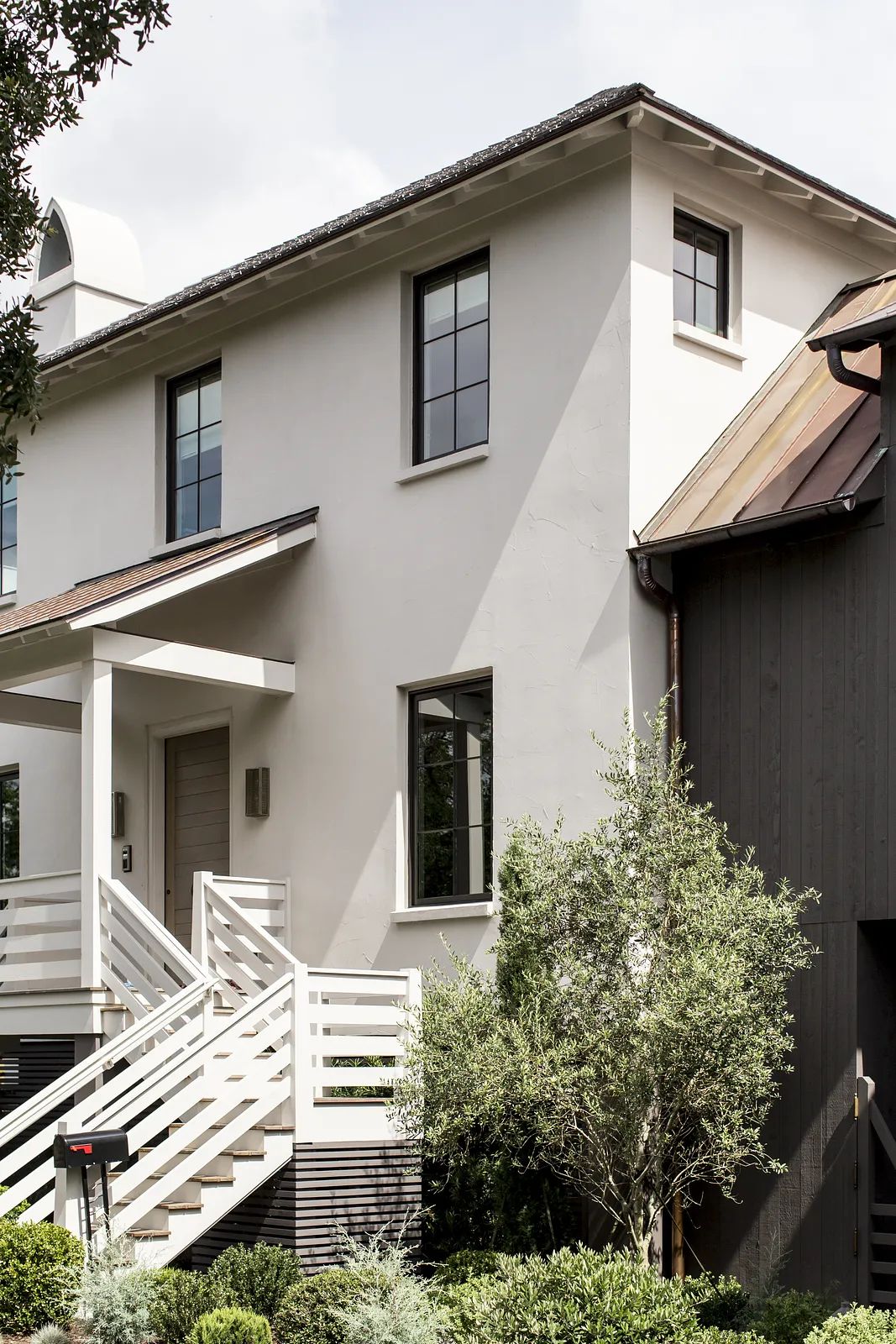Exterior front of a two-story house with beige stucco, dark wood accents, covered porch, and landscaping.