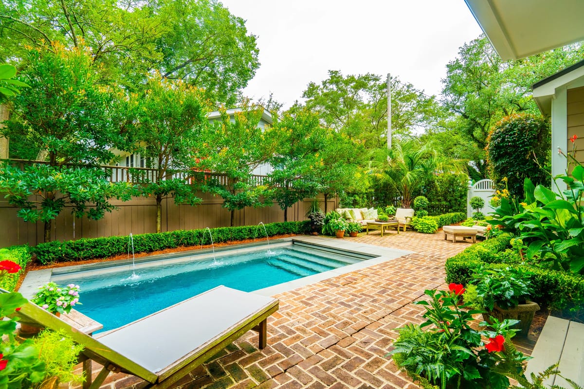 Garden with swimming pool, brick patio, lounge chairs, and abundant greenery.