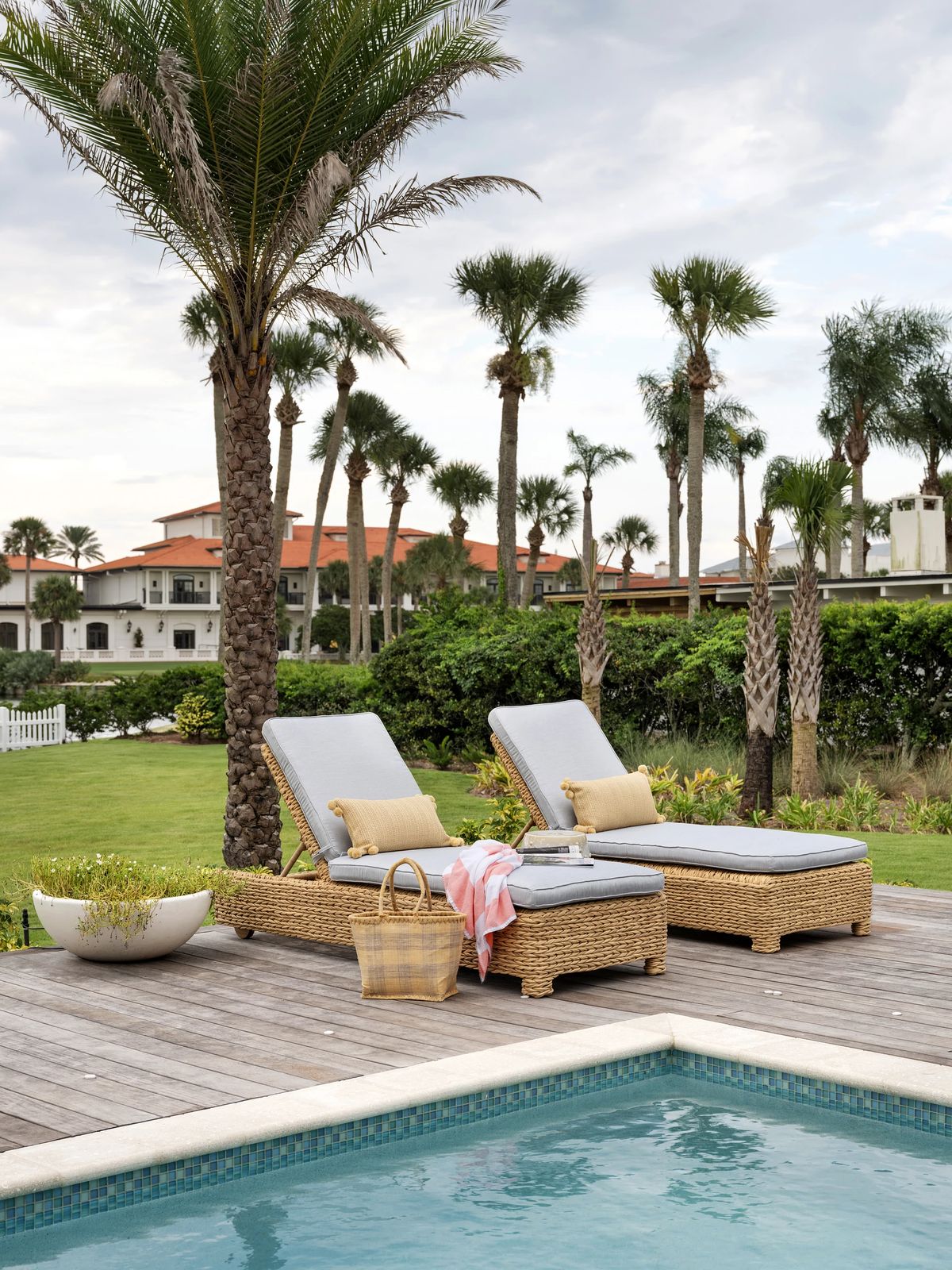 Patio with lounge chairs, pool, palm trees, and woven basket.