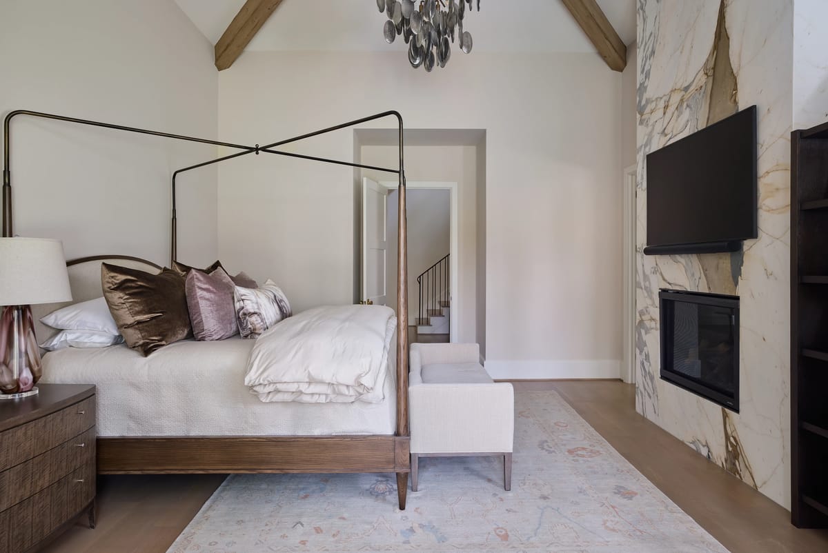 Bedroom with canopy bed, nightstands, armchair, patterned rug, marble accent wall, and mounted television