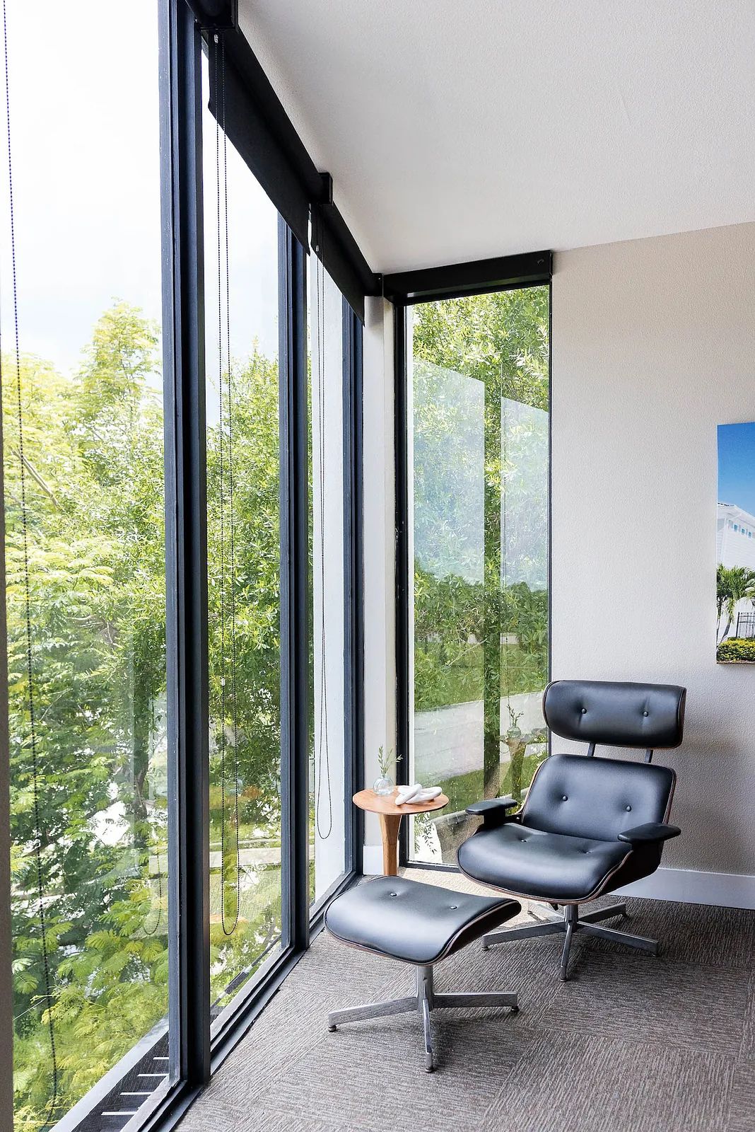 Seating area with black leather chair, ottoman, side table, and large floor-to-ceiling windows.