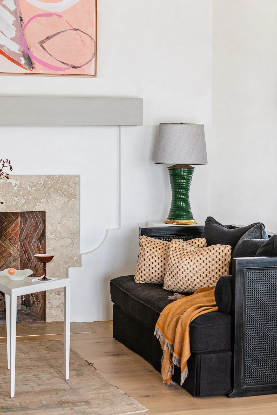 Living room with black sectional sofa, decorated side table, lamp, area rug, beige stone fireplace, and abstract art.