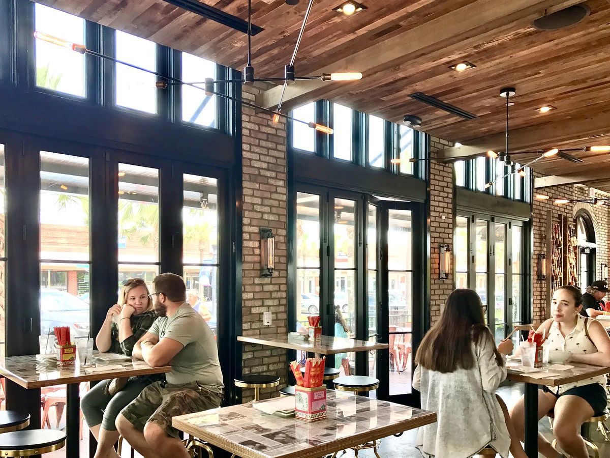 Dining room with metal and marble tables, brick walls, large glass doors, and wood ceiling.