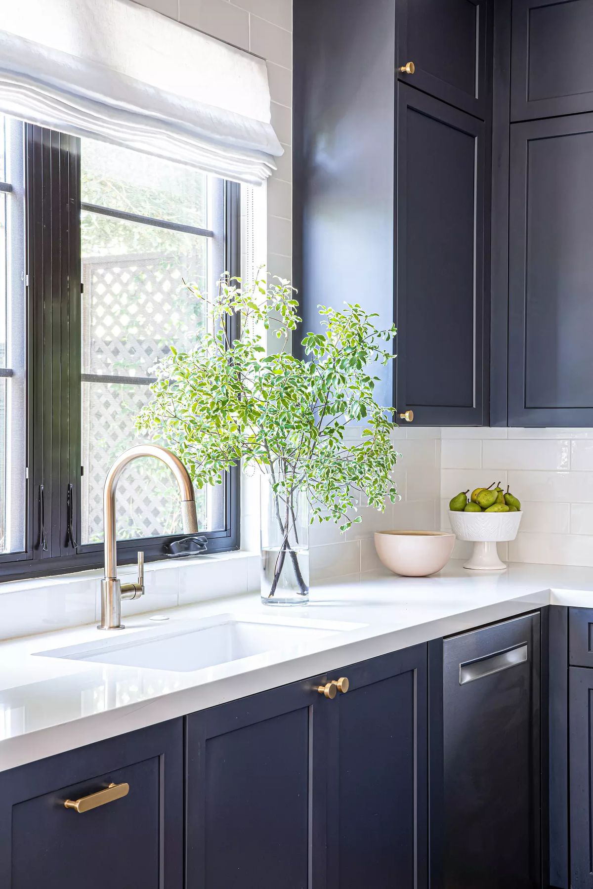 Kitchen with dark blue cabinetry, white countertop, sink, vase with greenery, and bowl with fruit.
