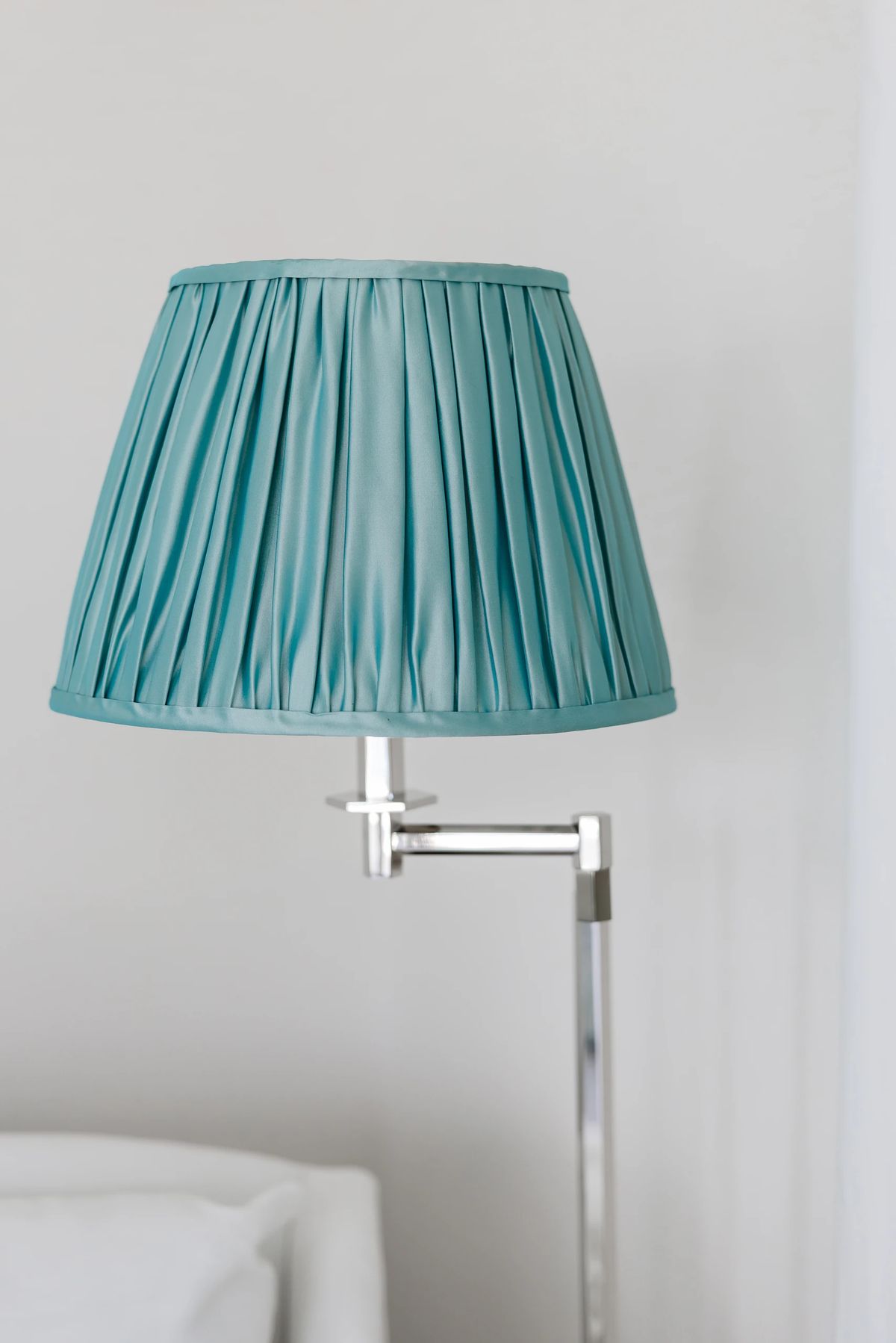 Teal pleated lamp shade on a silver lamp against a light gray wall.