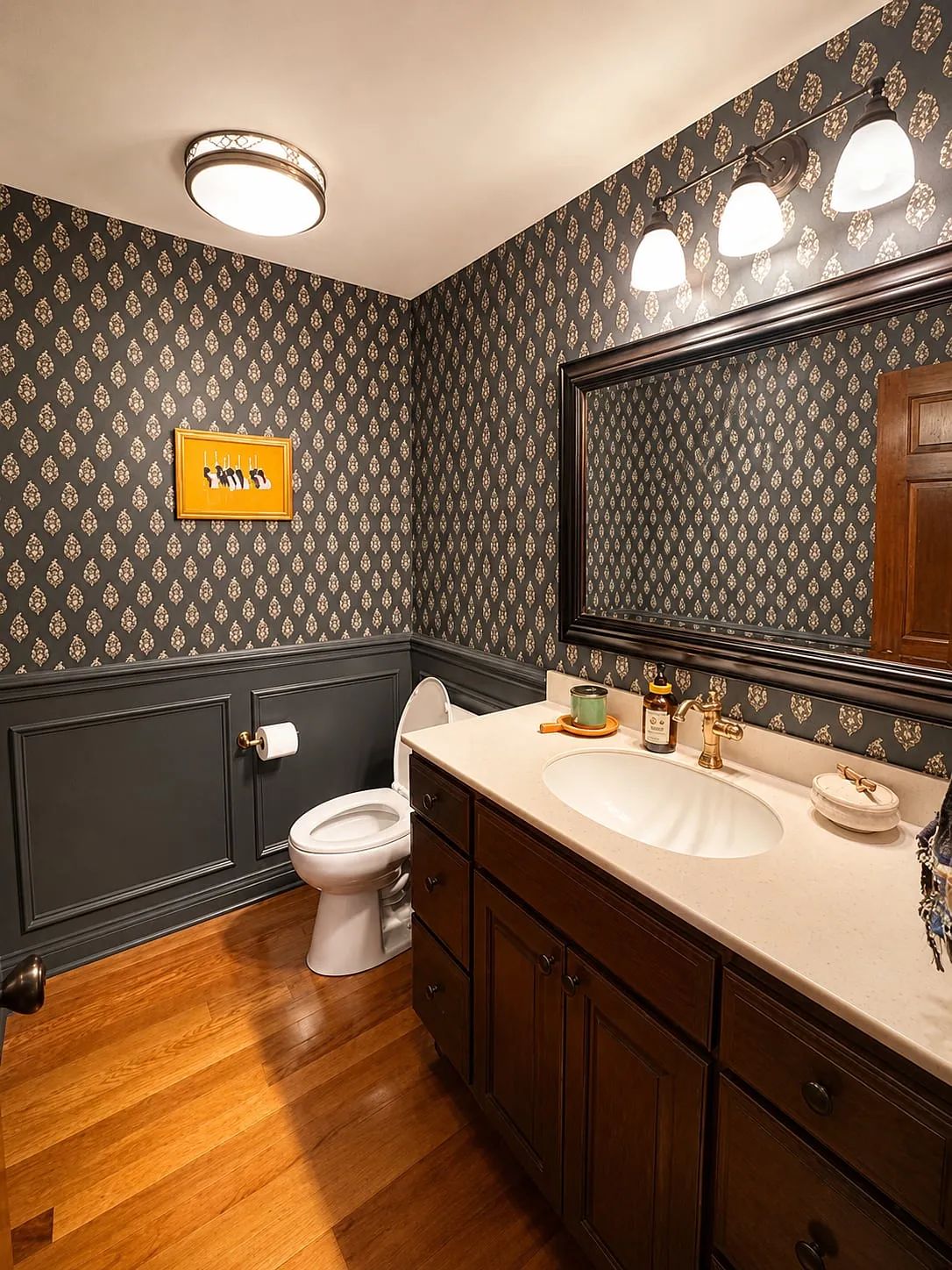 Powder room with dark wood vanity, sink, large mirror, white toilet, and patterned wallpaper.