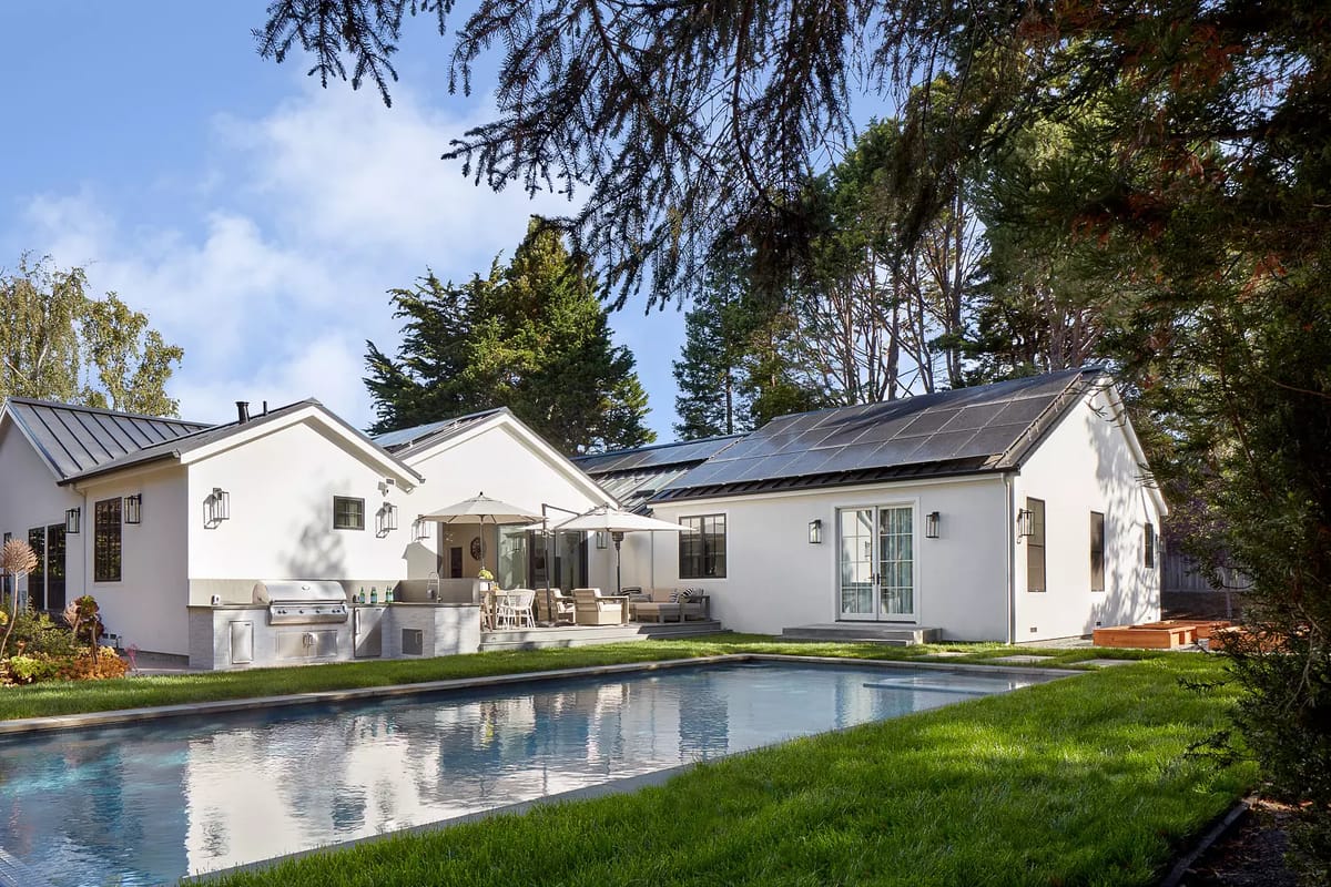 Exterior rear view with swimming pool, patio, outdoor furniture, and barbecue grill surrounded by grass and trees.