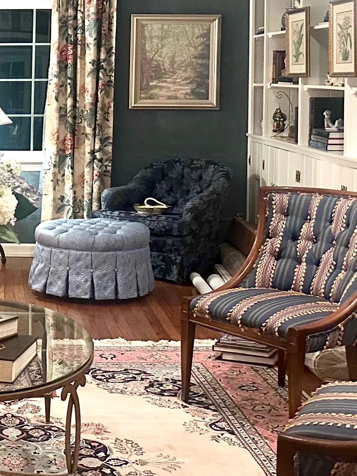 Living room with patterned rug, glass coffee table, striped chair, blue ottoman, and built-in bookshelf.