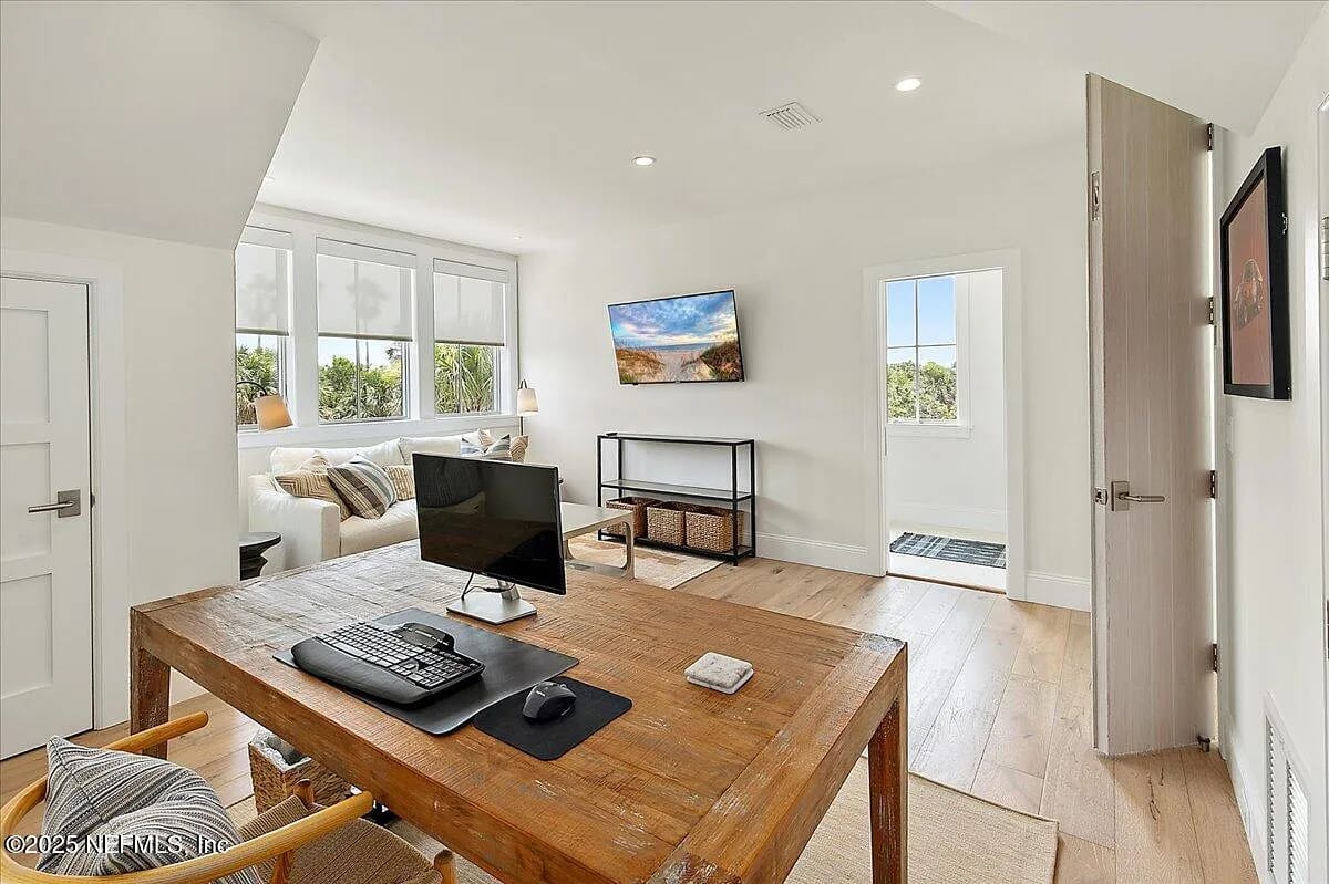 Office with wooden desk, computer, sofa, television, and large windows for natural light.