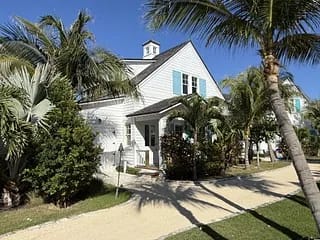House exterior with white siding, blue shutters, palm trees, and a sandy path.