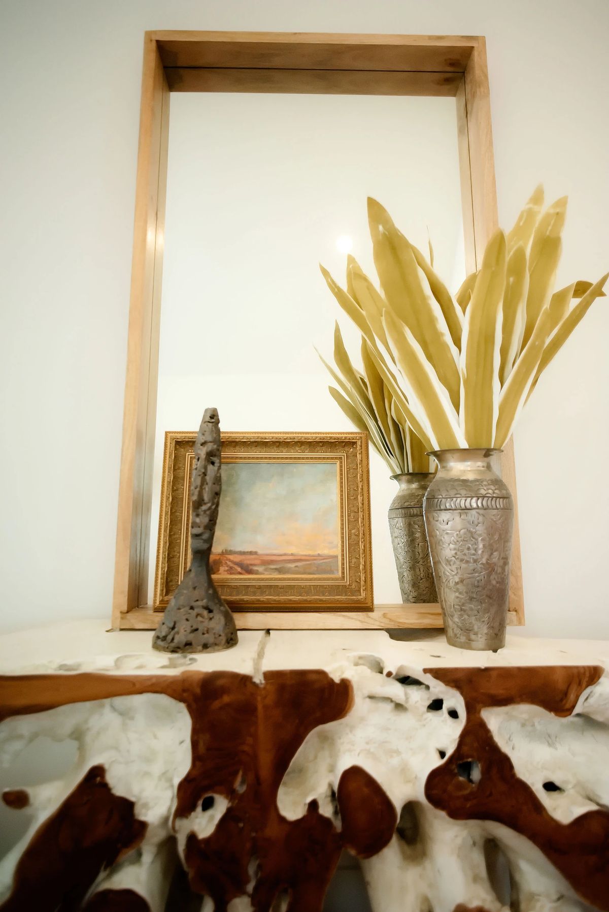 Decor arrangement with mirror frame, painting, sculpture, metallic vases, and driftwood base.