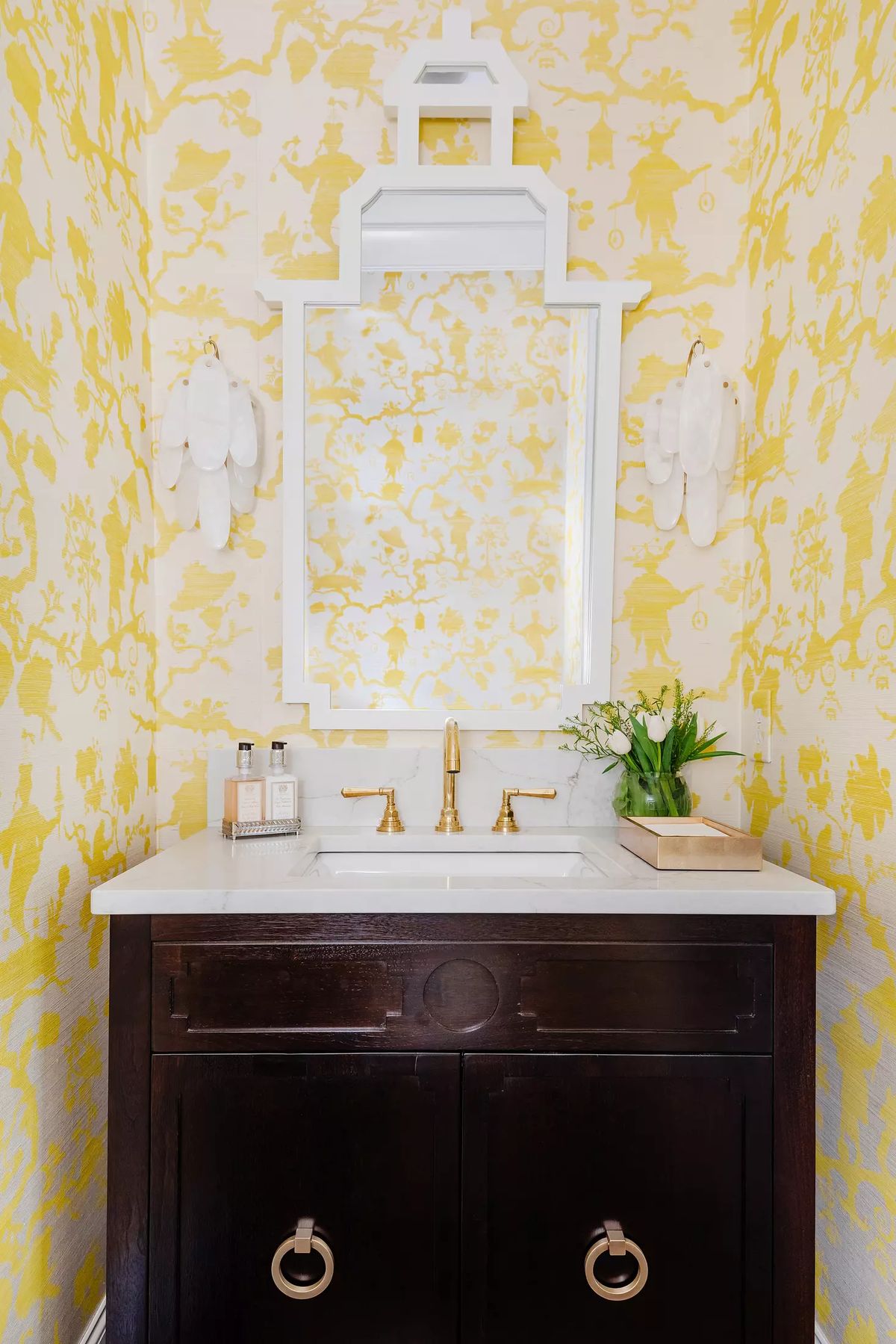 Powder room with dark wood vanity, white countertop, yellow floral wallpaper, and gold faucets.