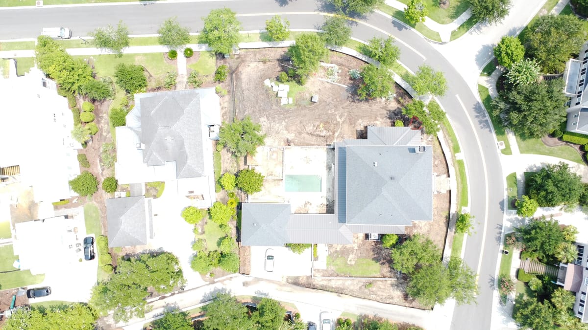 Aerial view of residential area with multiple houses, landscaping, and visible swimming pool outline.