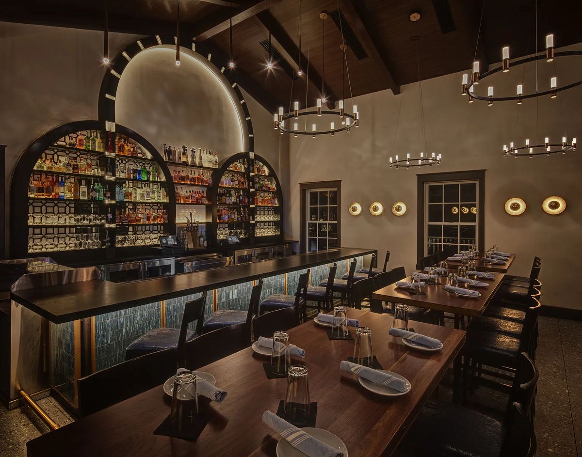 Dining room with long wooden table, black chairs, built-in bar, and circular chandeliers.