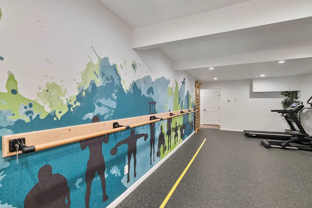 Fitness area with wall mural, barre, treadmill, potted plant, and recessed lighting