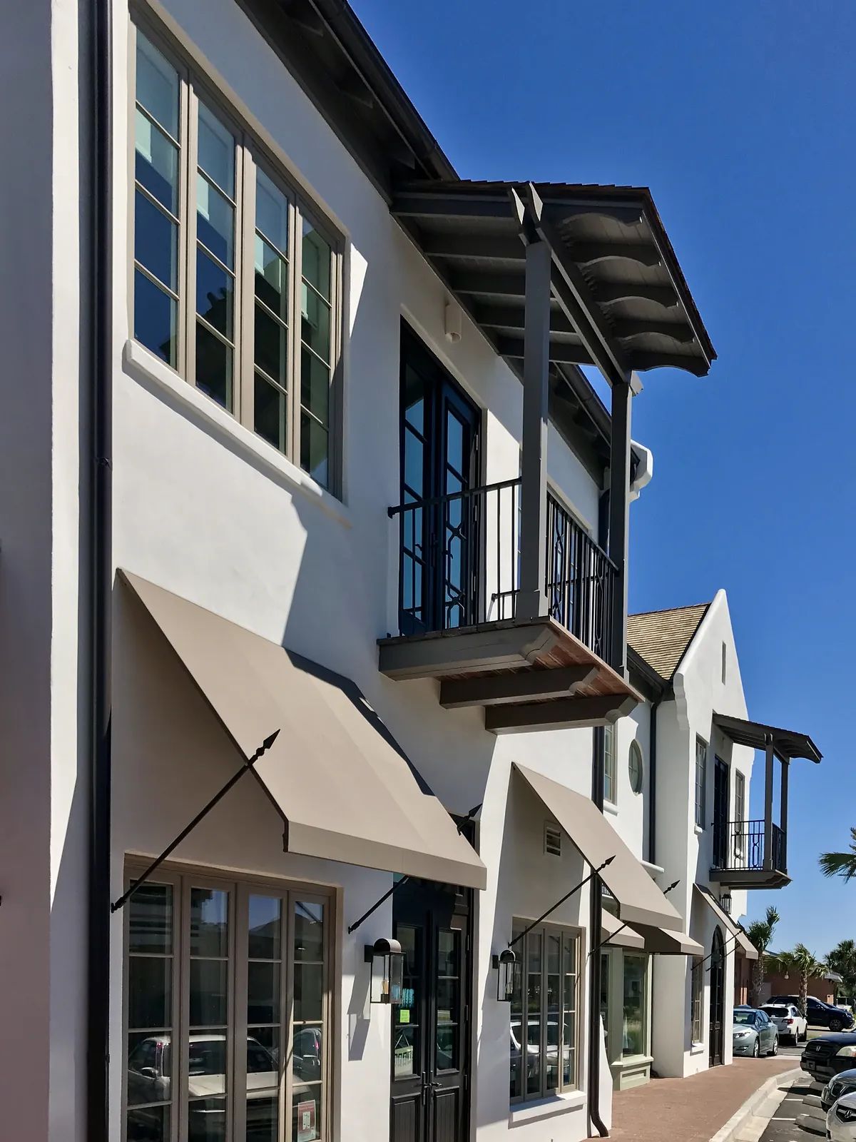Exterior front view of a building with multiple windows, balconies, awnings, and stucco finish.