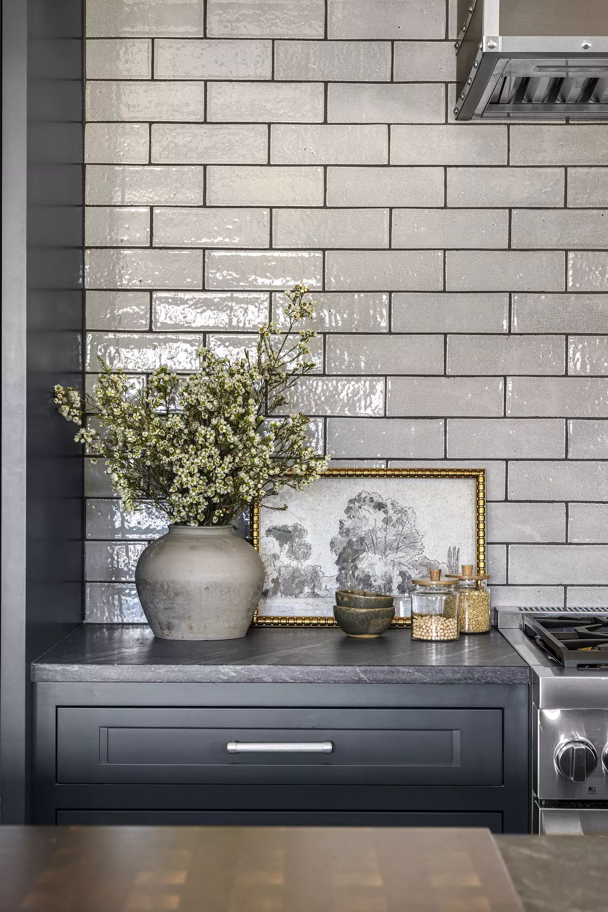 Kitchen with gray subway tile, dark cabinetry, countertop decor, and stainless steel range hood.
