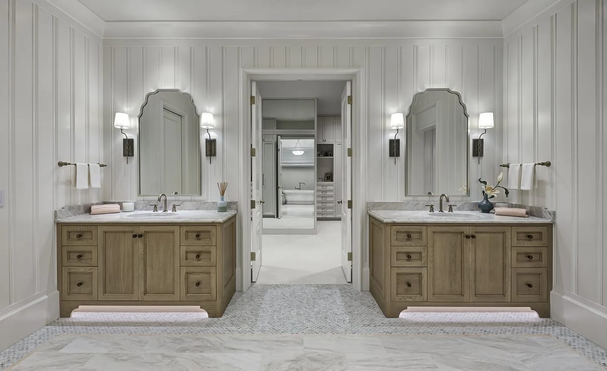 Bathroom with two vanities, marble countertops, large mirrors, paneled walls, and tiled flooring.