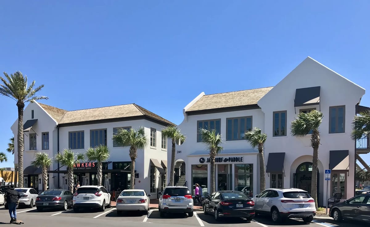 Exterior view of two commercial buildings with signs, palm trees, and parked cars.