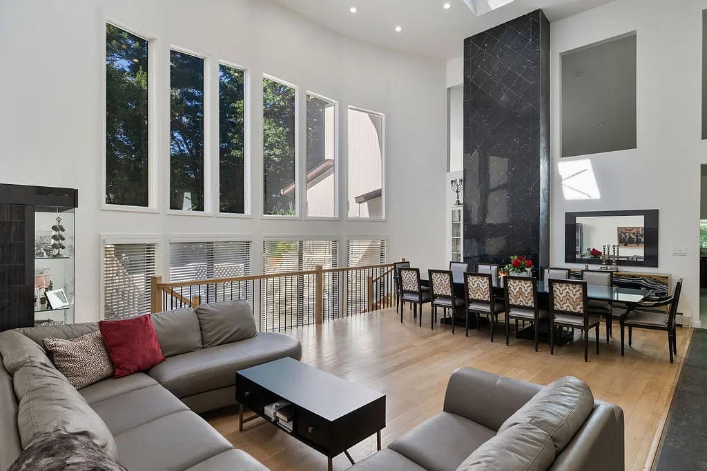 Living room with gray sectional sofa, black coffee table, dining area, and stone feature wall with large windows.
