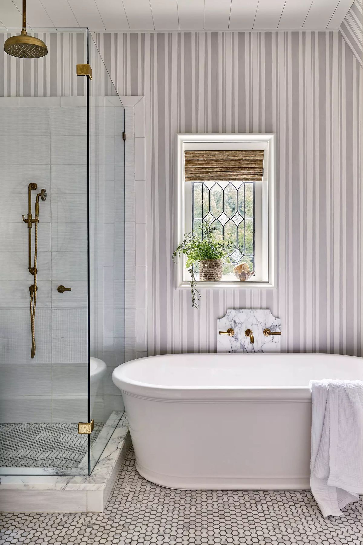Bathroom with freestanding tub, glass shower, hexagonal tile, striped wallpaper, and a window with a plant
