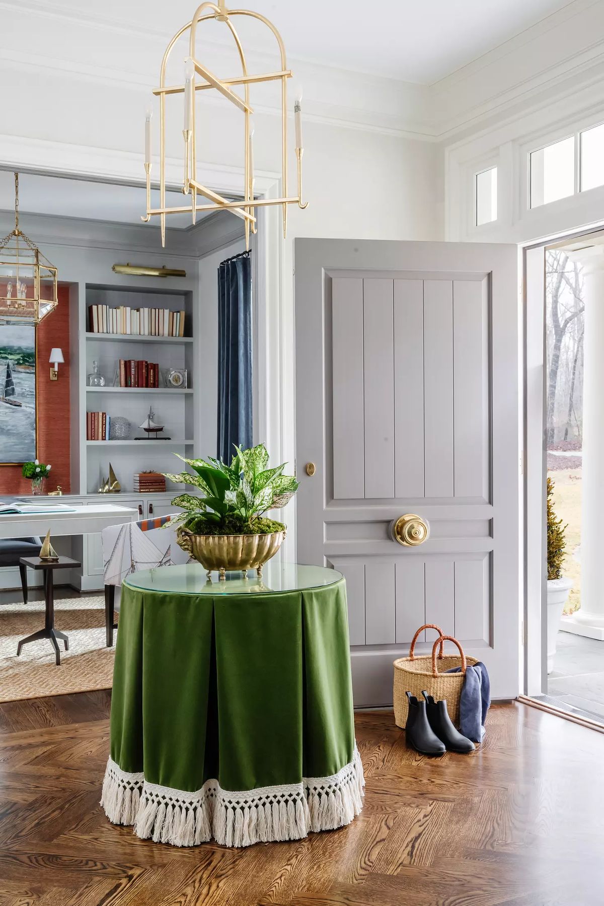 Foyer with round table, plant, gray door, built-in bookshelf, and green curtains.