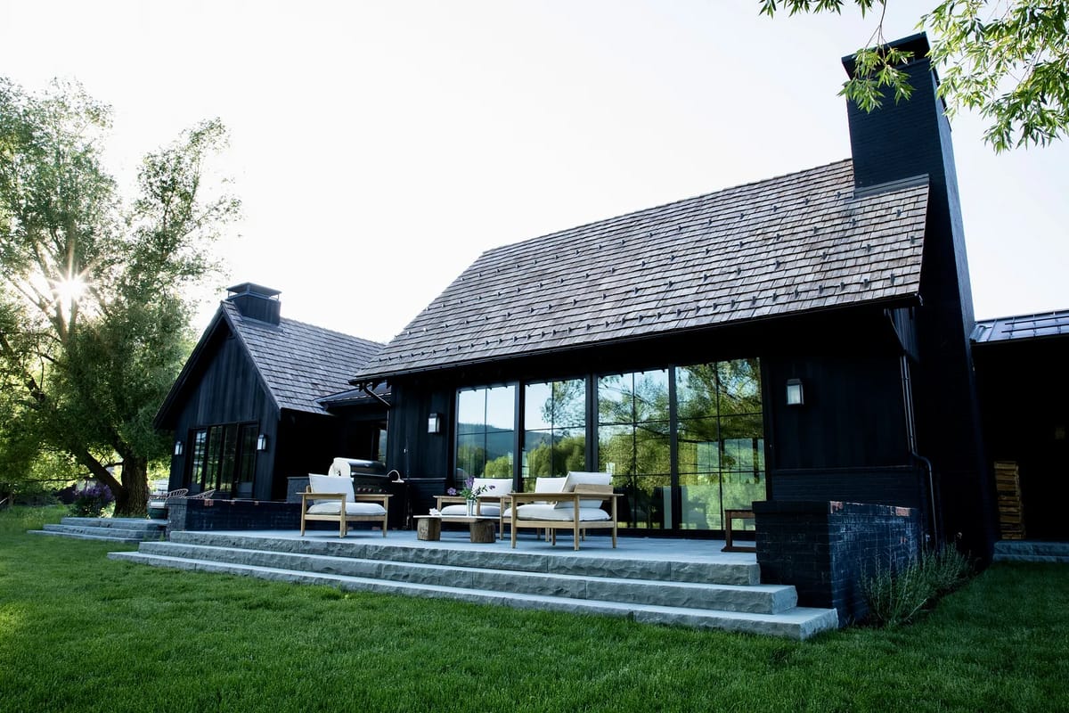 Rear exterior view with glass sliding door, outdoor seating, stone steps, and grass area