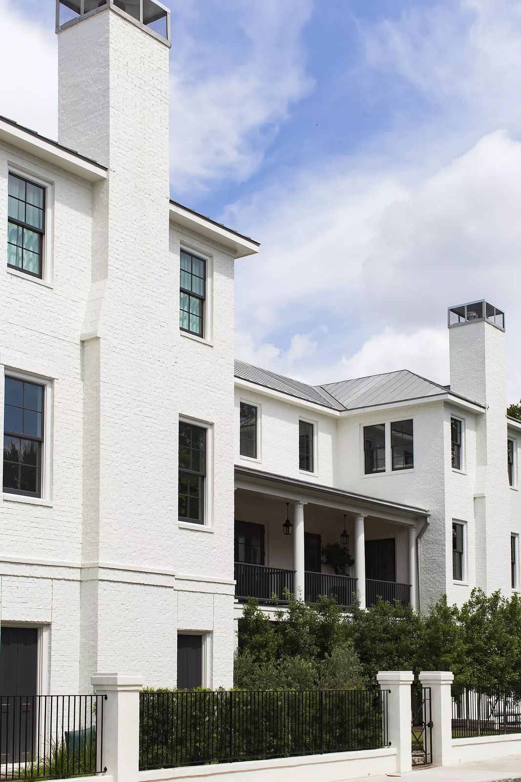Exterior view of a white brick house with large windows, chimneys, porch, and landscaping.