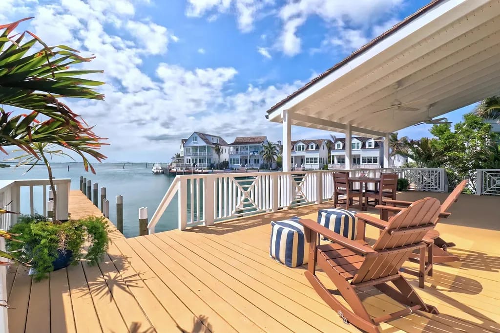 Outdoor deck with wooden flooring, adirondack chairs, dining table, and views of the water.