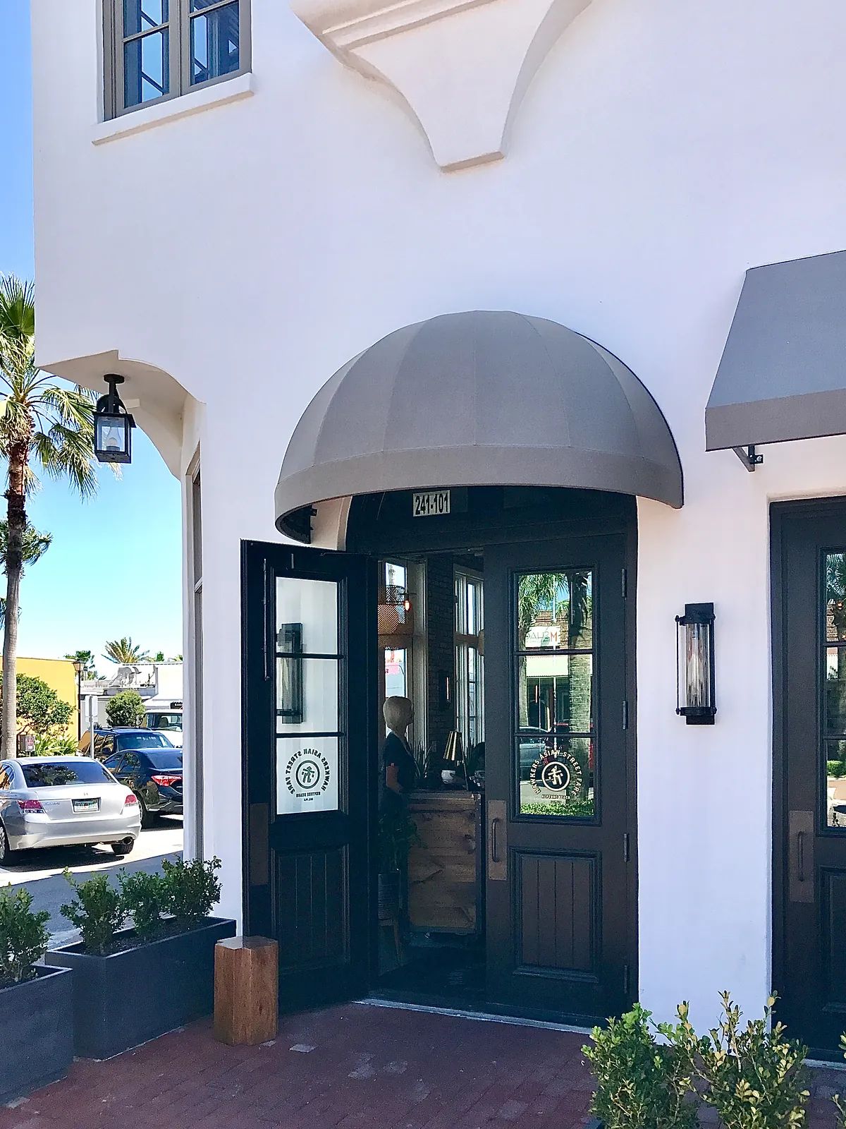 Exterior front entrance with arched awning, black double doors, wall sconces, and potted plants.