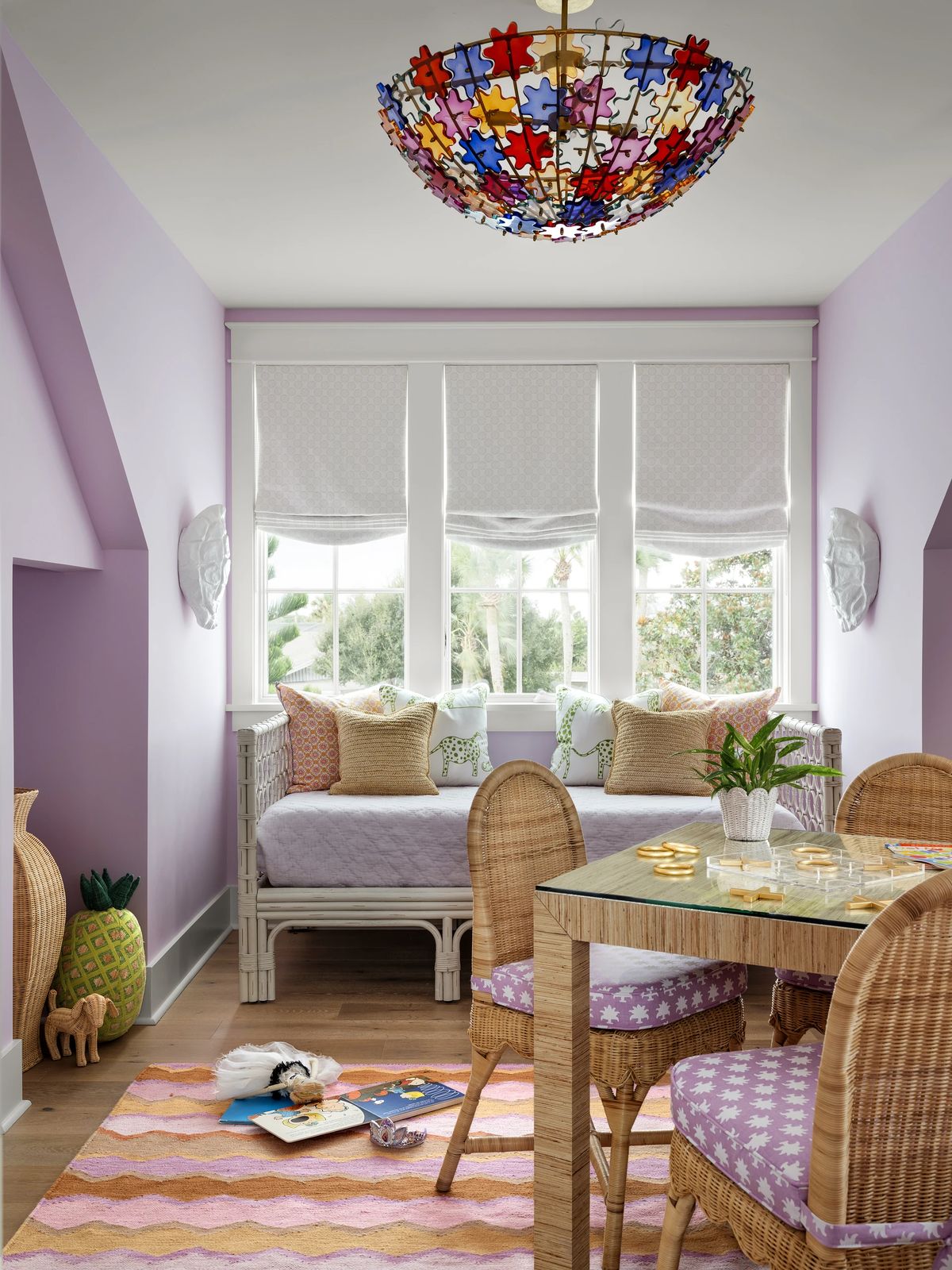 Small room with daybed, round table, wicker chairs, colorful rug, and puzzle-themed chandelier.