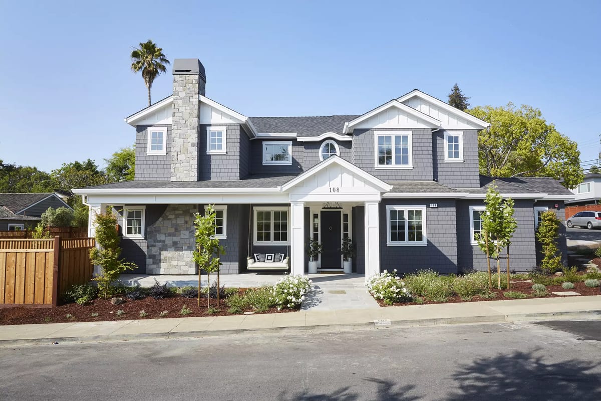Front exterior of a house with stone façade, pathway, porch, and landscaped garden beds.
