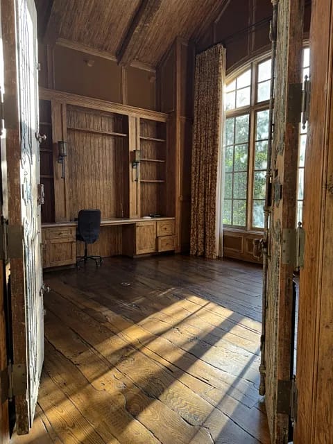Office with wooden flooring, built-in cabinetry, desk, chair, and large windows with curtains.