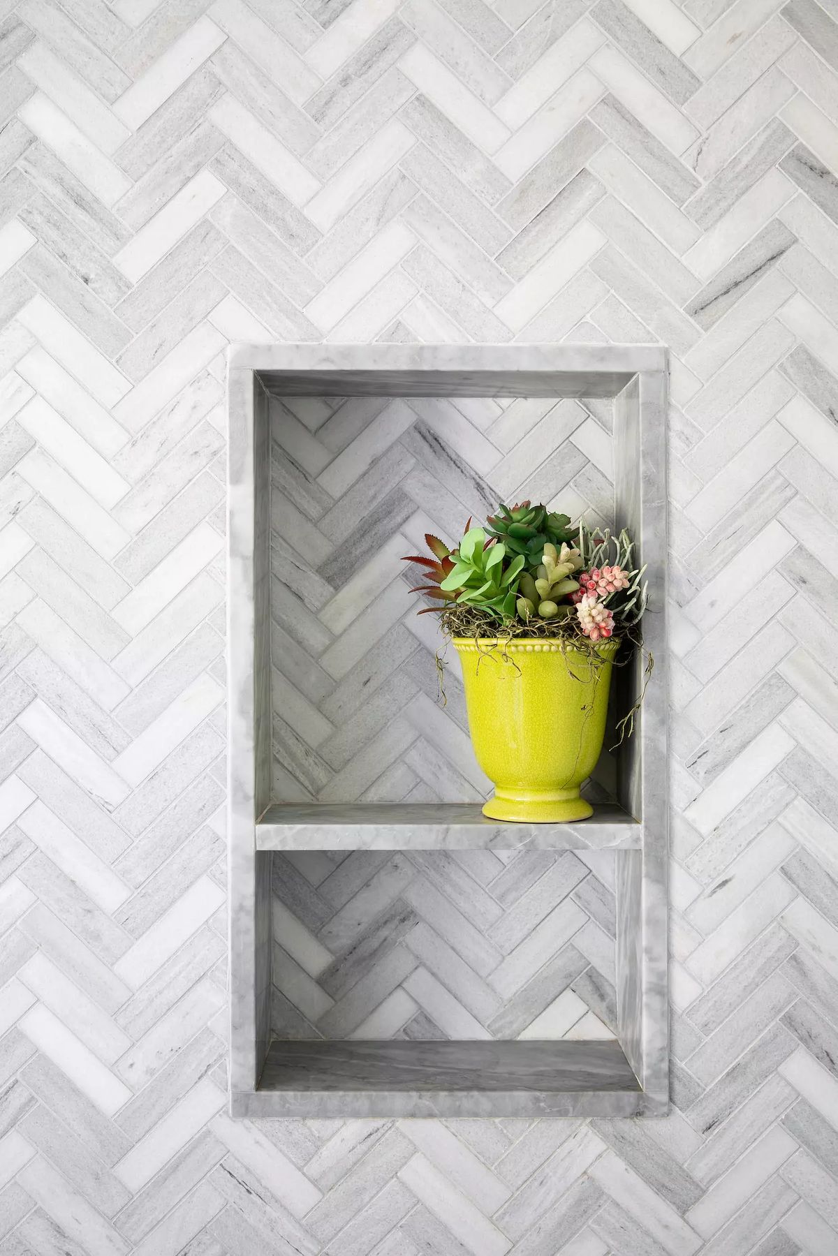 Recessed gray marble shelf with succulents on a herringbone patterned gray and white wall.