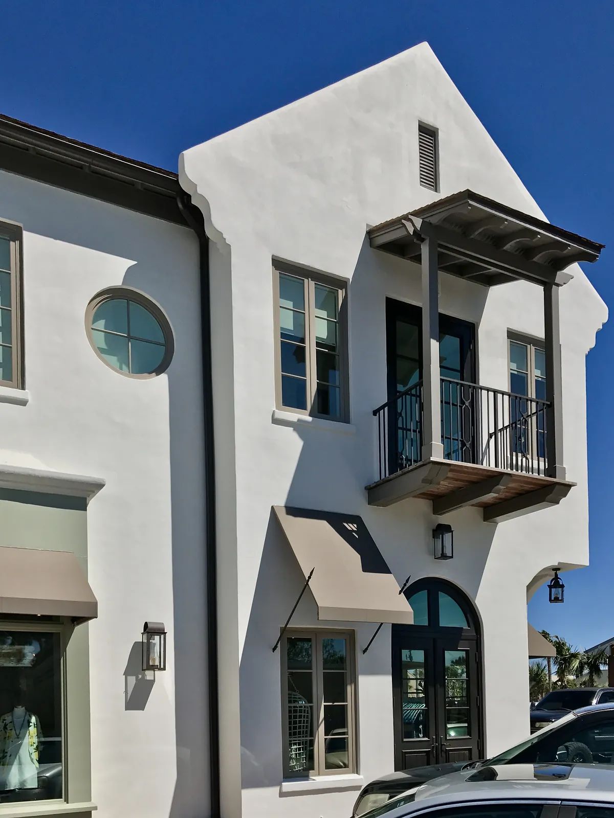 Exterior view of a building with white stucco, circular windows, balcony, and decorative lanterns.