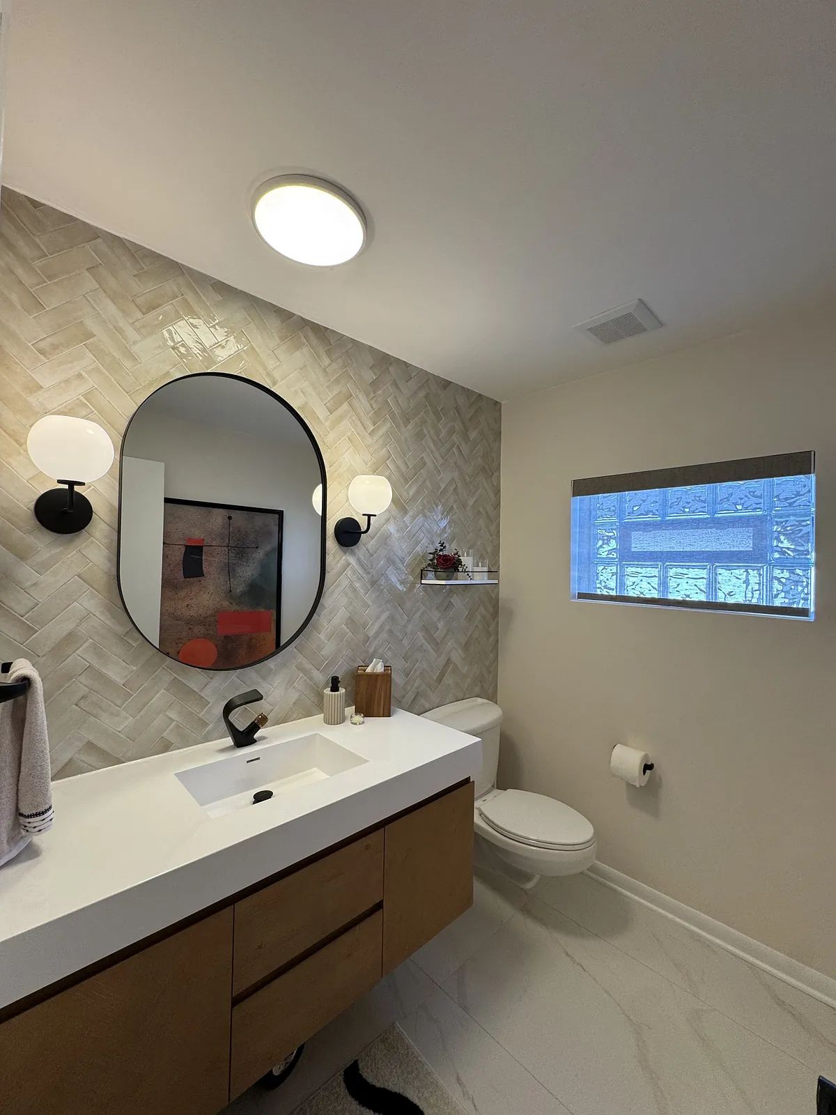 Bathroom with floating vanity, double basin sink, round mirror, beige herringbone tile, and natural light.
