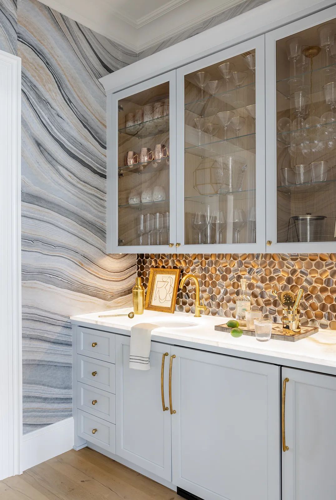 Kitchen with light blue cabinets, white countertop, stone backsplash, gold faucet, and marble wall.